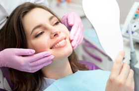 Cosmetic dental patient holding hand mirror, smiling at her reflection